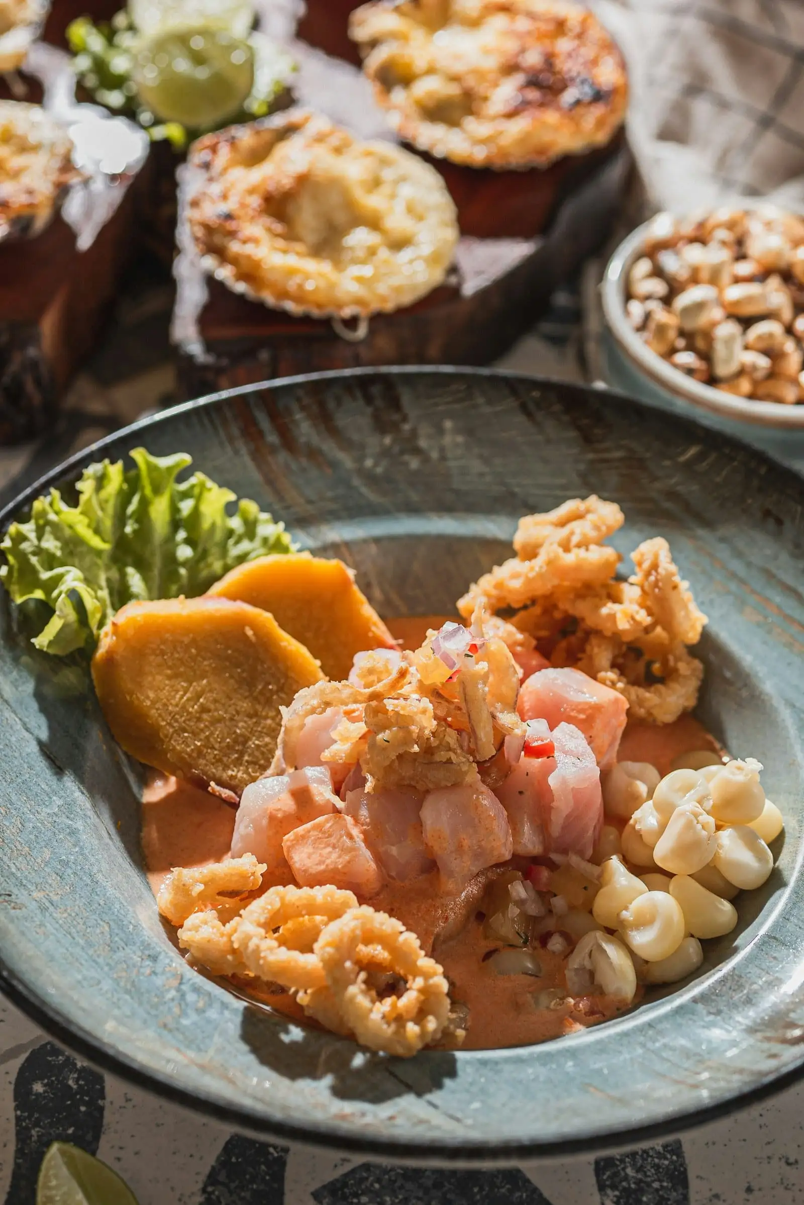 Ceviche con calamares fritos, camote, choclo y lechuga en un plato de cerámica
