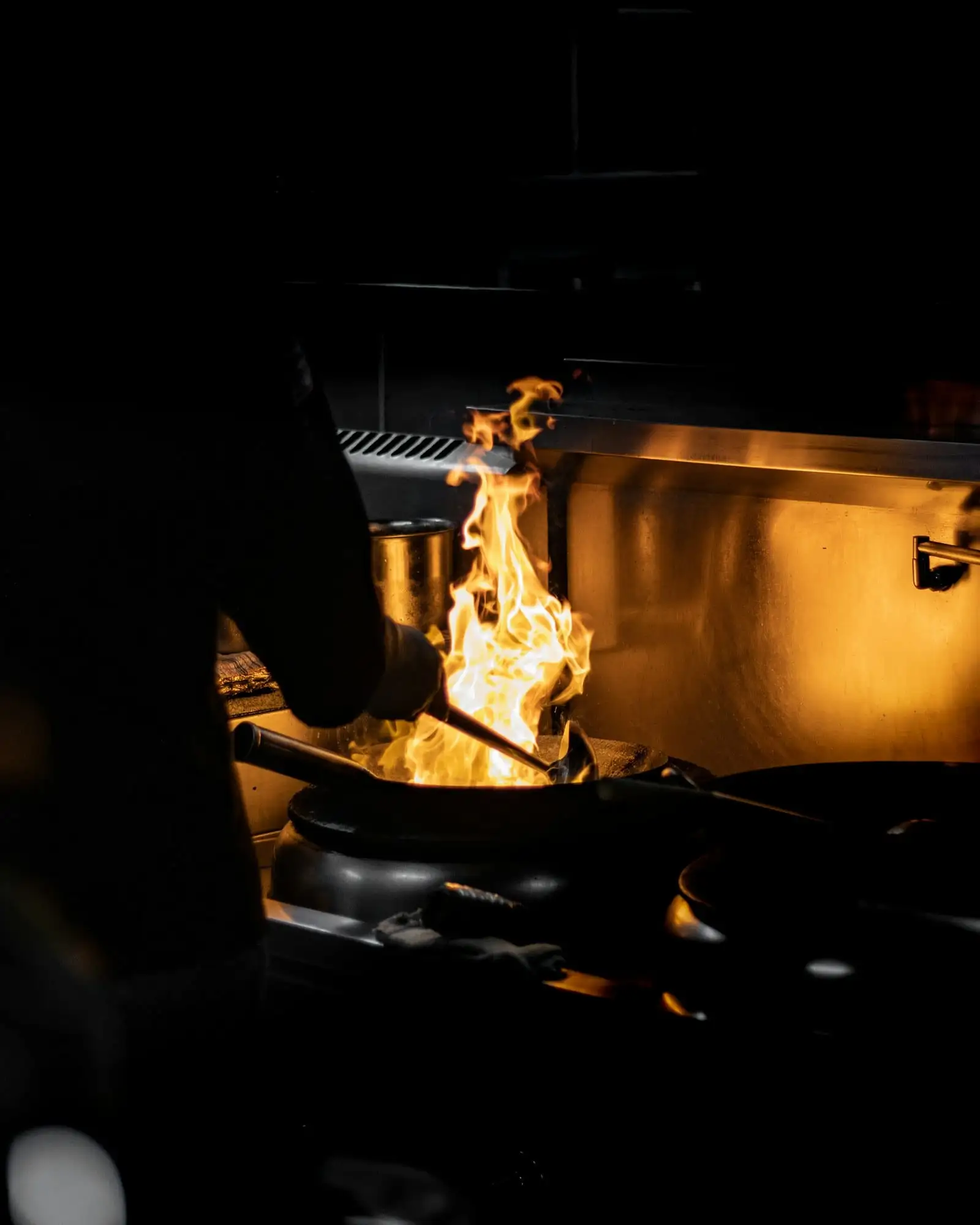 Cocinero saltando en el wok con una llamarada, en la cocina a media luz
