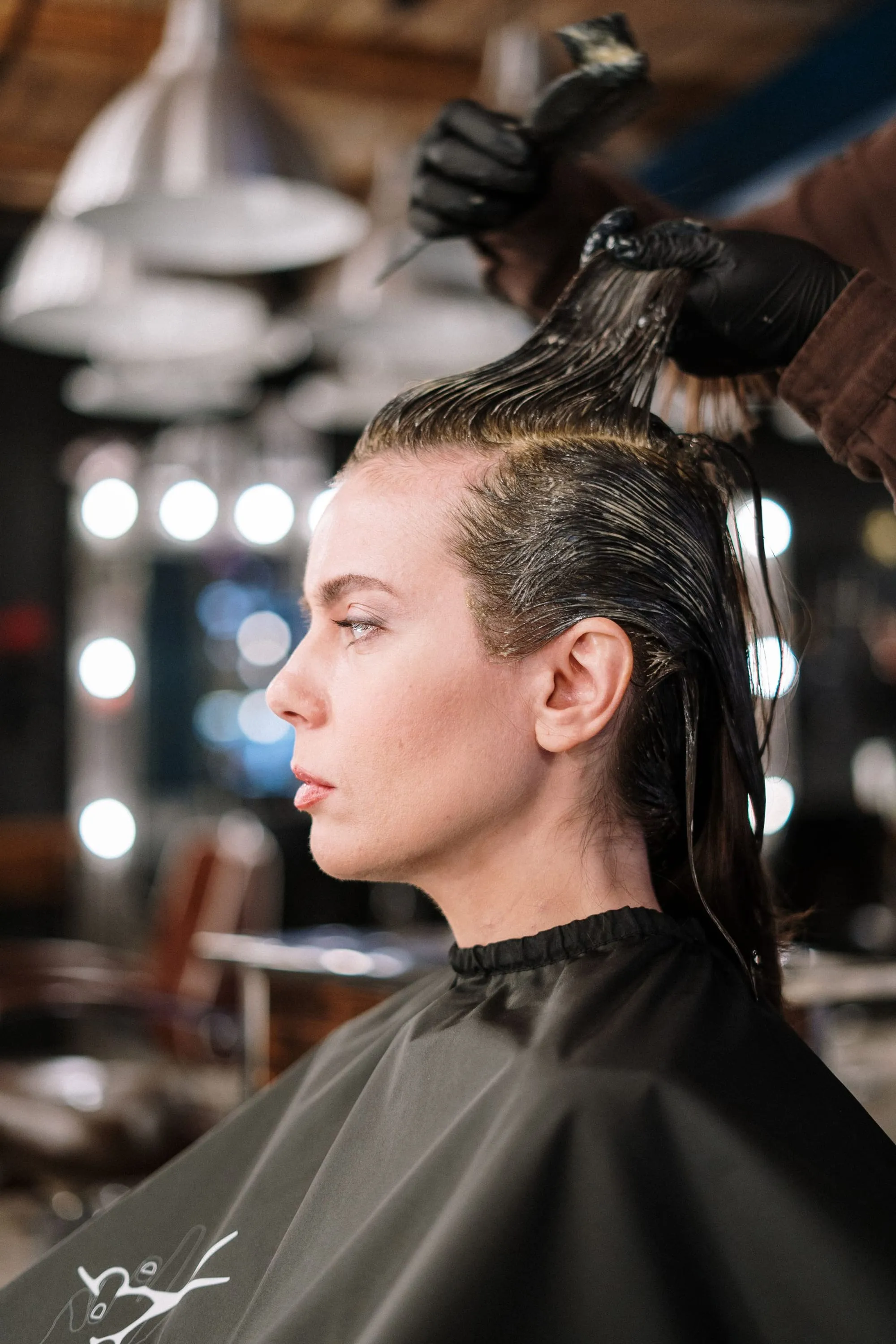 Clienta en un salón con espejos iluminados mientras le aplican color en el cabello