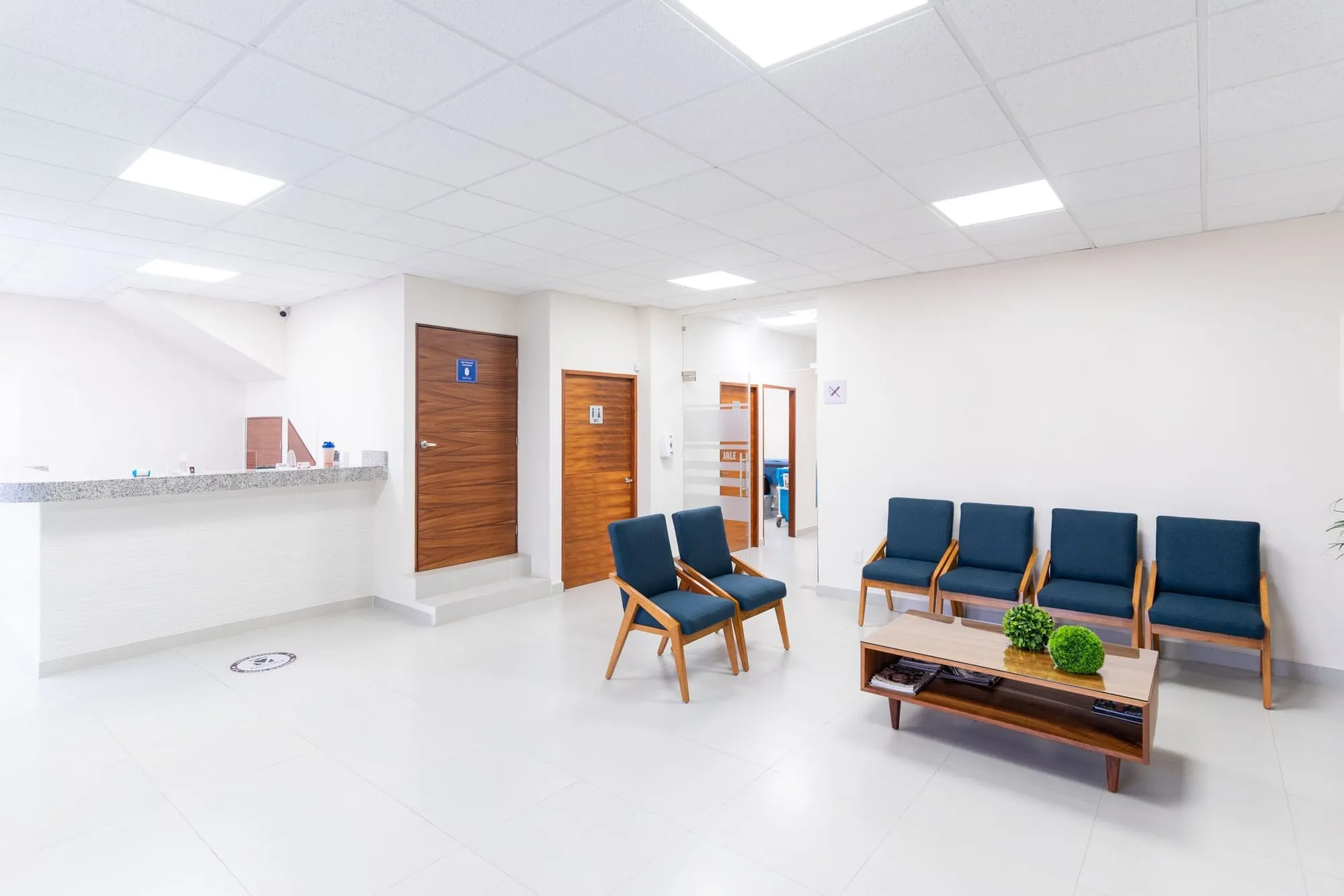 Sala de espera luminosa de un consultorio, con sillas azules y puertas de madera
