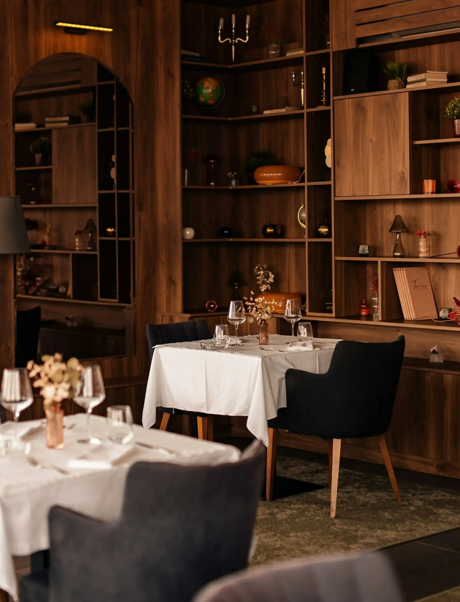 Salón con mesas de mantel blanco, copas y estantes de madera